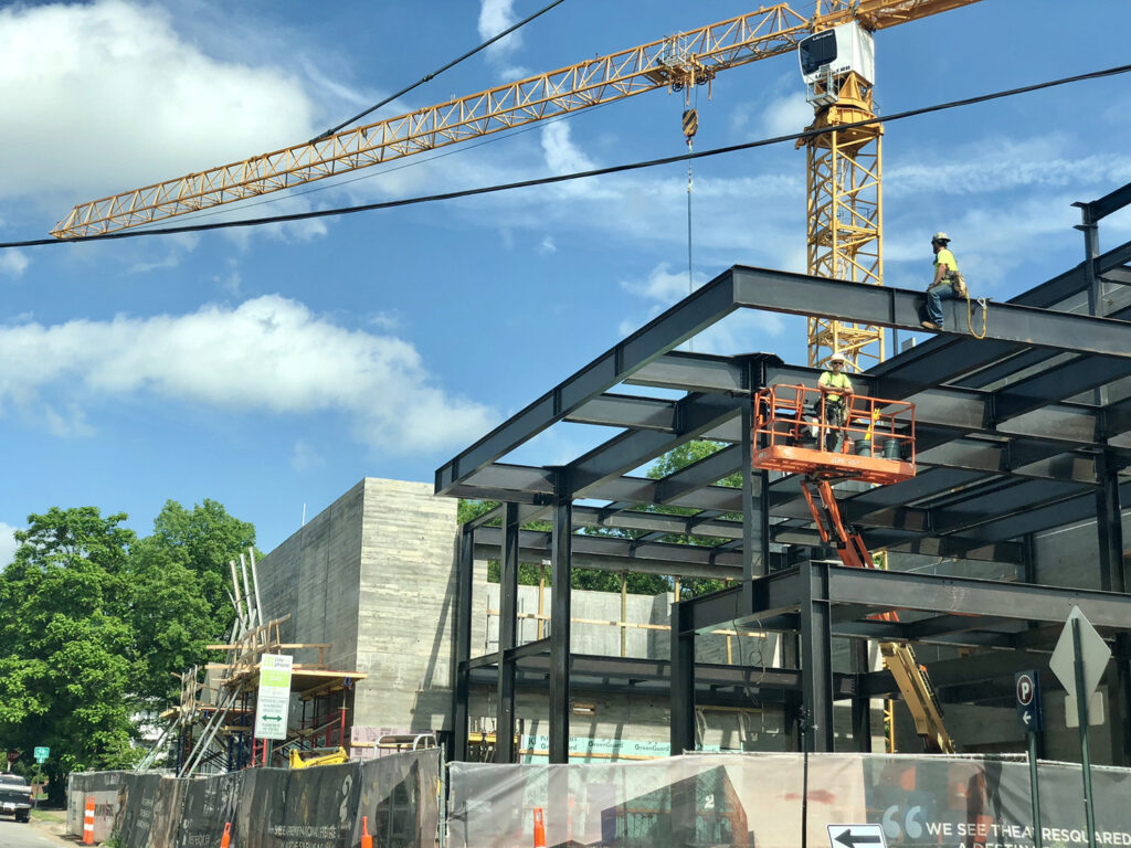 Construction workers amidst a body steel structure with a crane behind them.