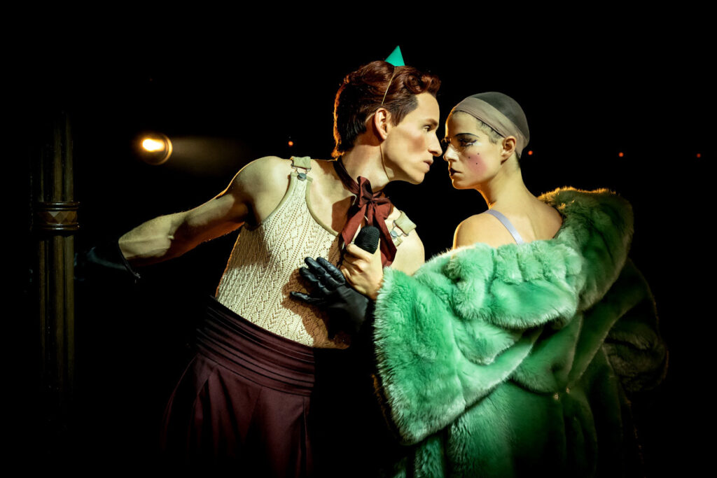 Eddie Redmayne and Jessie Buckley in costume share an intense look.
