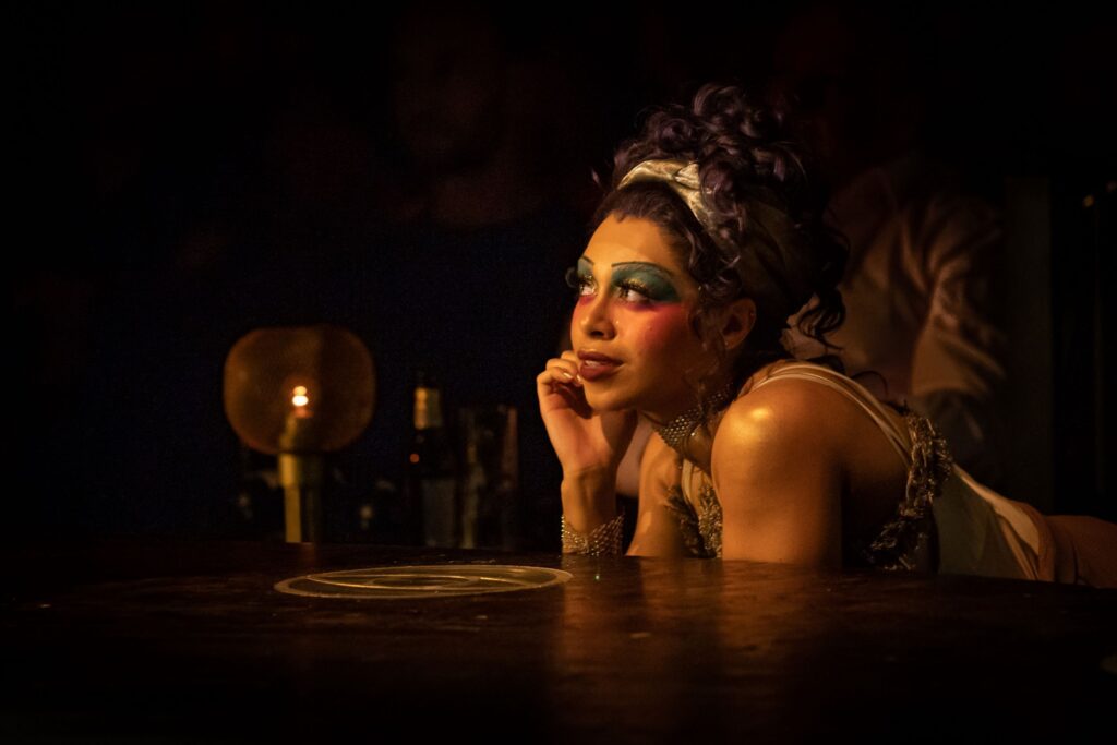 An actor with colorful makeup looks off into the distance.