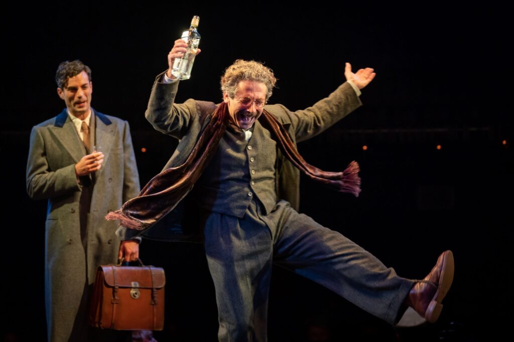 A Cabaret actor in formal clothes kicks out a leg with a bottle raised.
