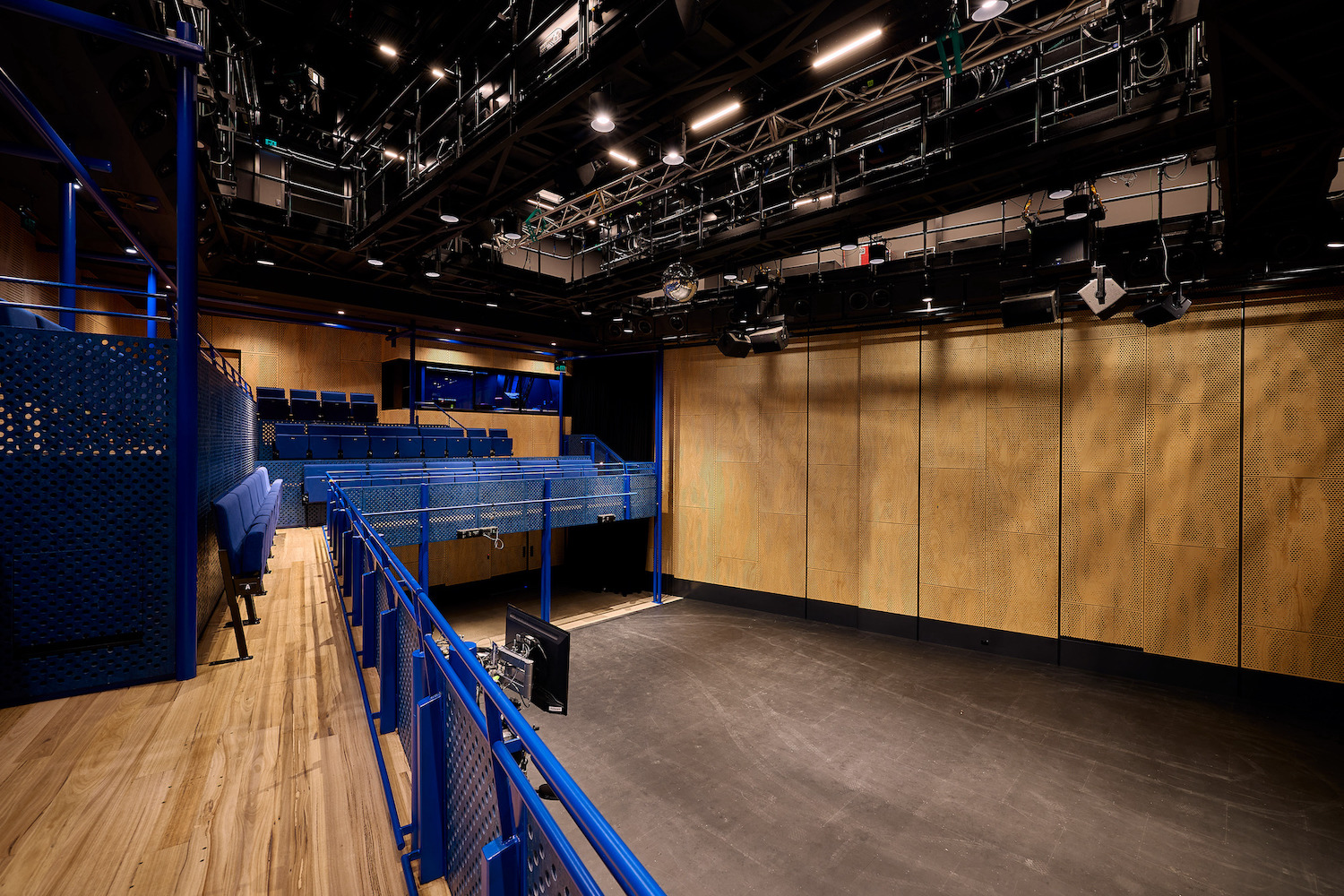 The catwalk and interior of a performance space with bright blue seats and rails, and wood patterned finishes.