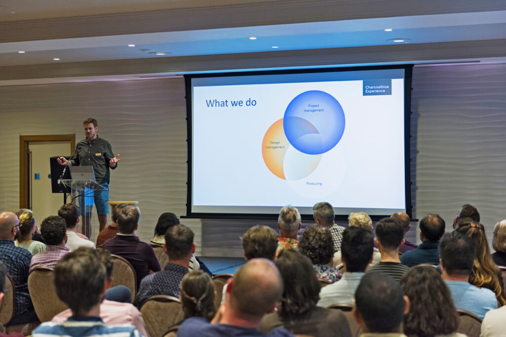 Ian on stage presenting a slide about what Charcoalblue does.