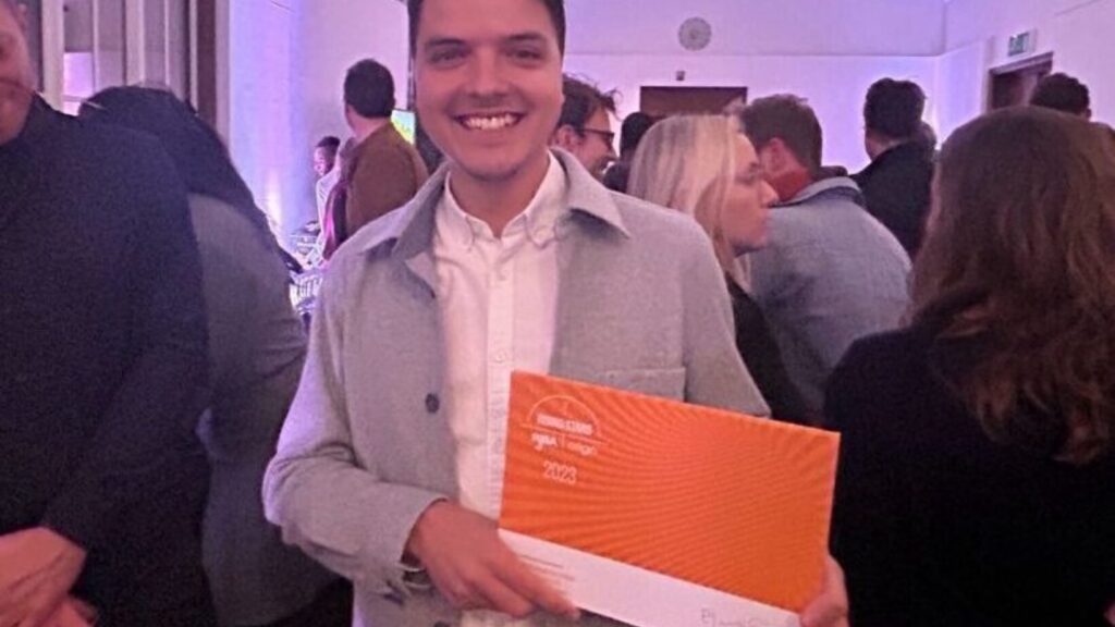 Oli holding an orange award certificate.
