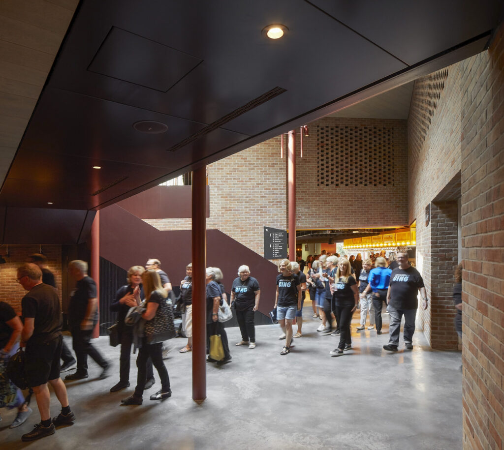 A crowd moves through a foyer with brick, concrete and reddish-brown finishes.