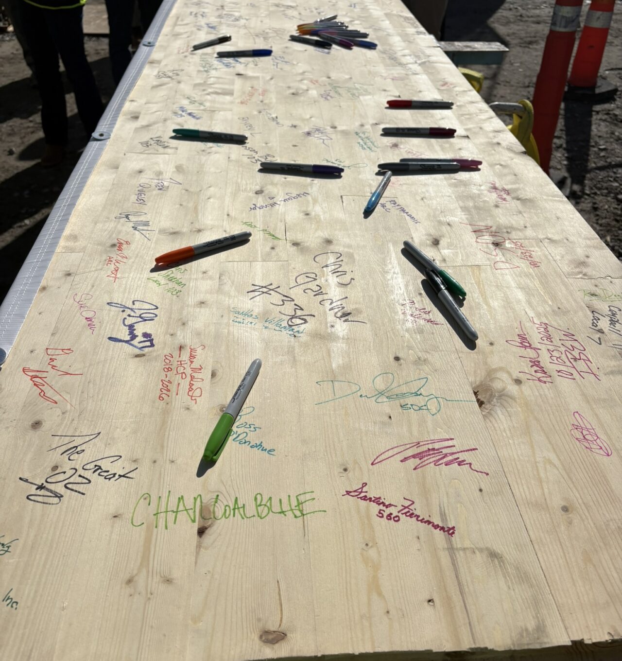 Teams members sign a beam in colorful Sharpie at American Repertory Theater construction site.