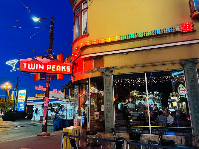 Exterior view of the glass windows of Twin Peaks Tavern. Illuminated and neon signage show the way in.