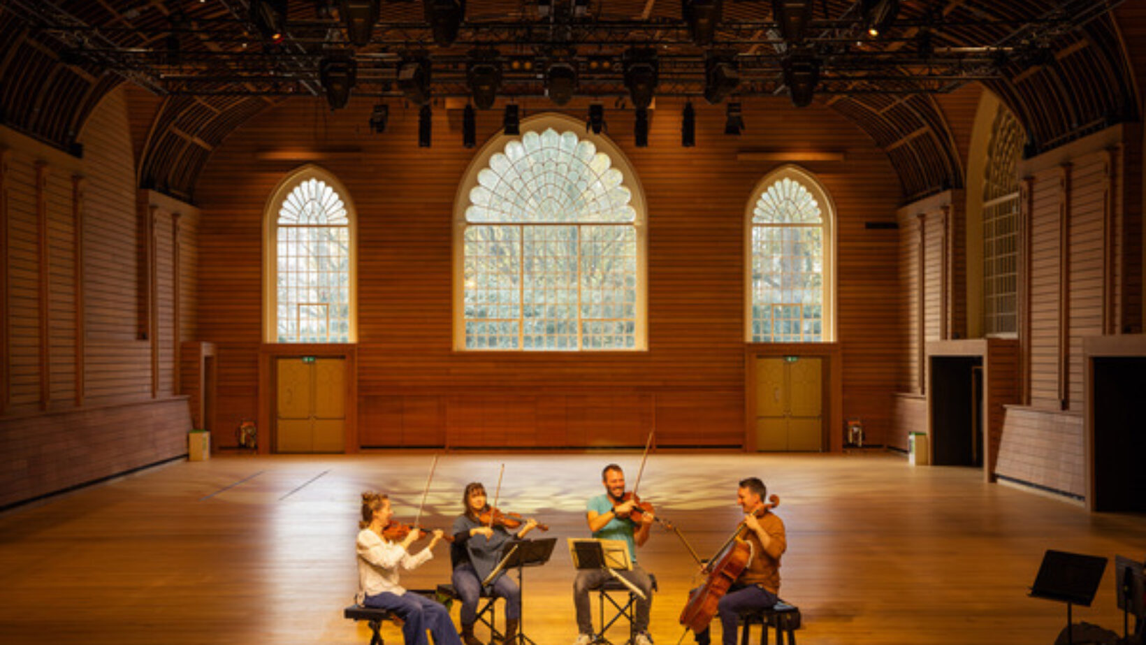 Performance space with three arched windows and string orchestra playing.