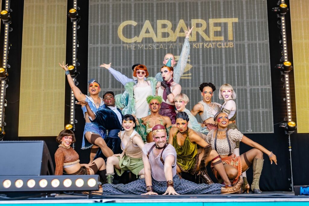 Cabaret performers on stage pose with arms outstretched.