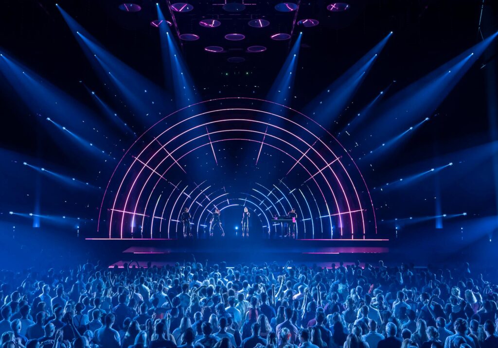 Performers under an illuminated arch and blue light. © Johan Persson