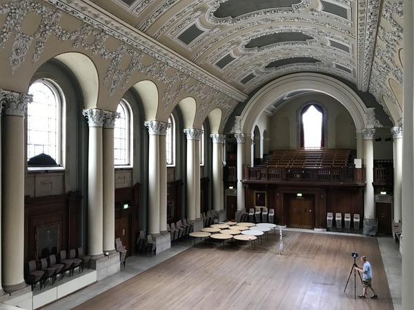 An arched hall with intricate decorative moulding along the ceiling and corinthian columns framing arched windows along its length.