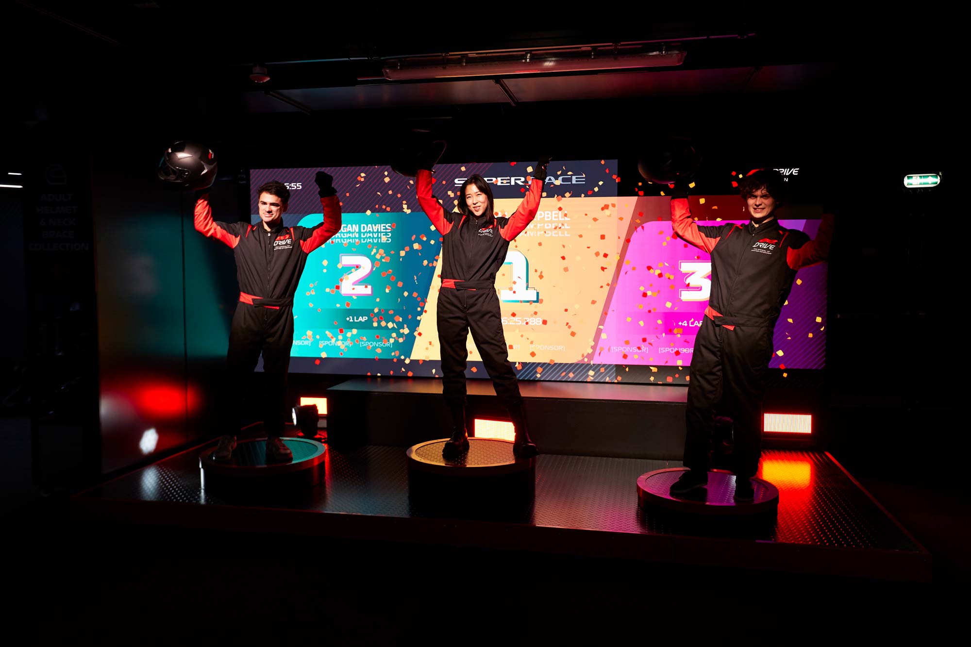 racers stand on the winner's podium. An LED screen displays first second and third place and their names, along with digital confetti. Photo by Pete Muller.
