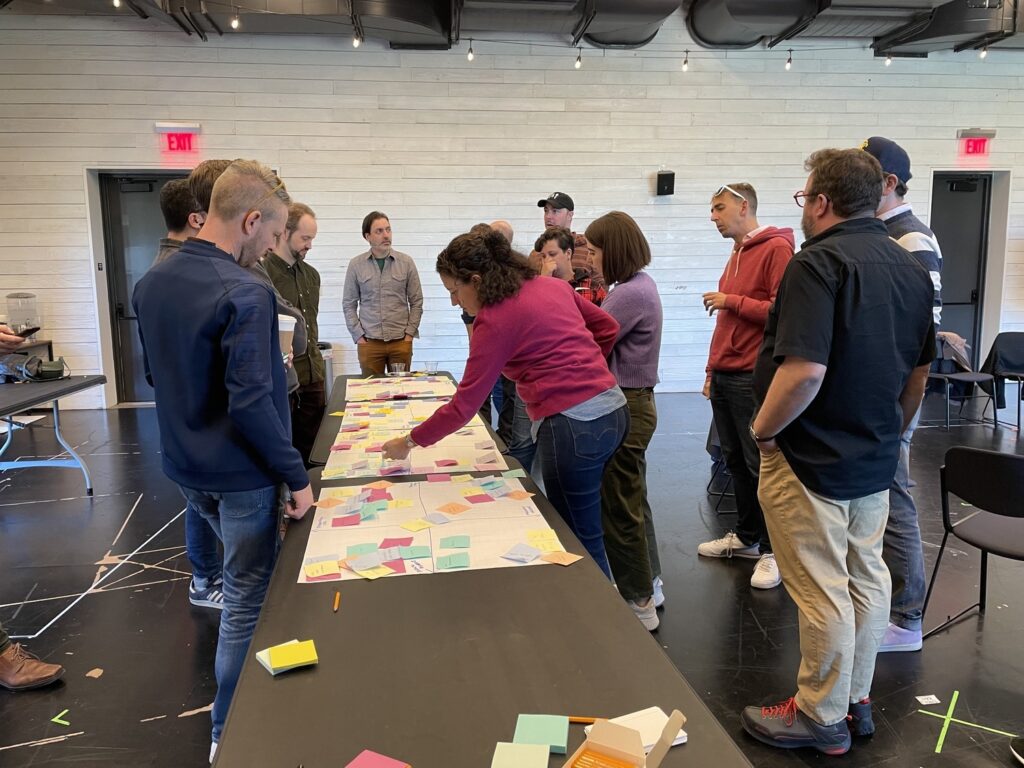 Team members gather around a table and arrange sticky notes into four quadrants.