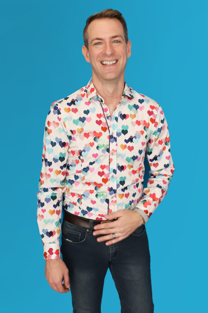 Portrait of Bradley Fritz in colorful heart-patterned shirt on a blue background.