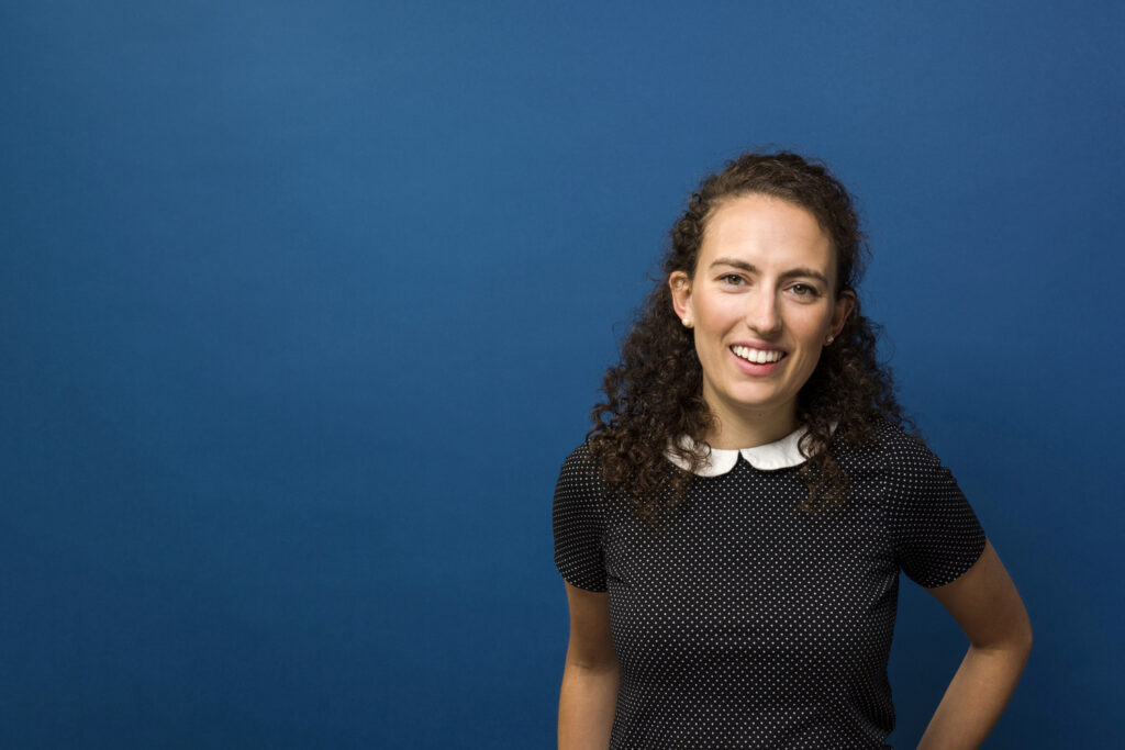 Kate Nolan portrait. She smiles on a blue background.