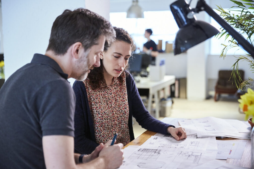 Kate Nolan and Peter Ruthven Hall in an office, looking at technical drawings.