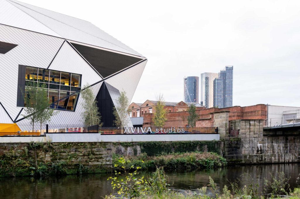 View of Aviva Studios sign over canal and the angular grey and white exterior of the building. Photo by Marco Cappelletti. Courtesy of OMA and Factory International.