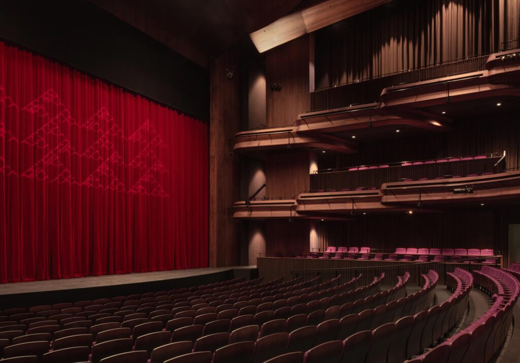 Curved rows of seating looking toward the red stage curtain. Photography courtesy of Jasmax.