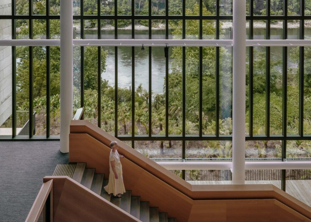 A person descends a staircase against a window onto the river. Photography courtesy of Jasmax.