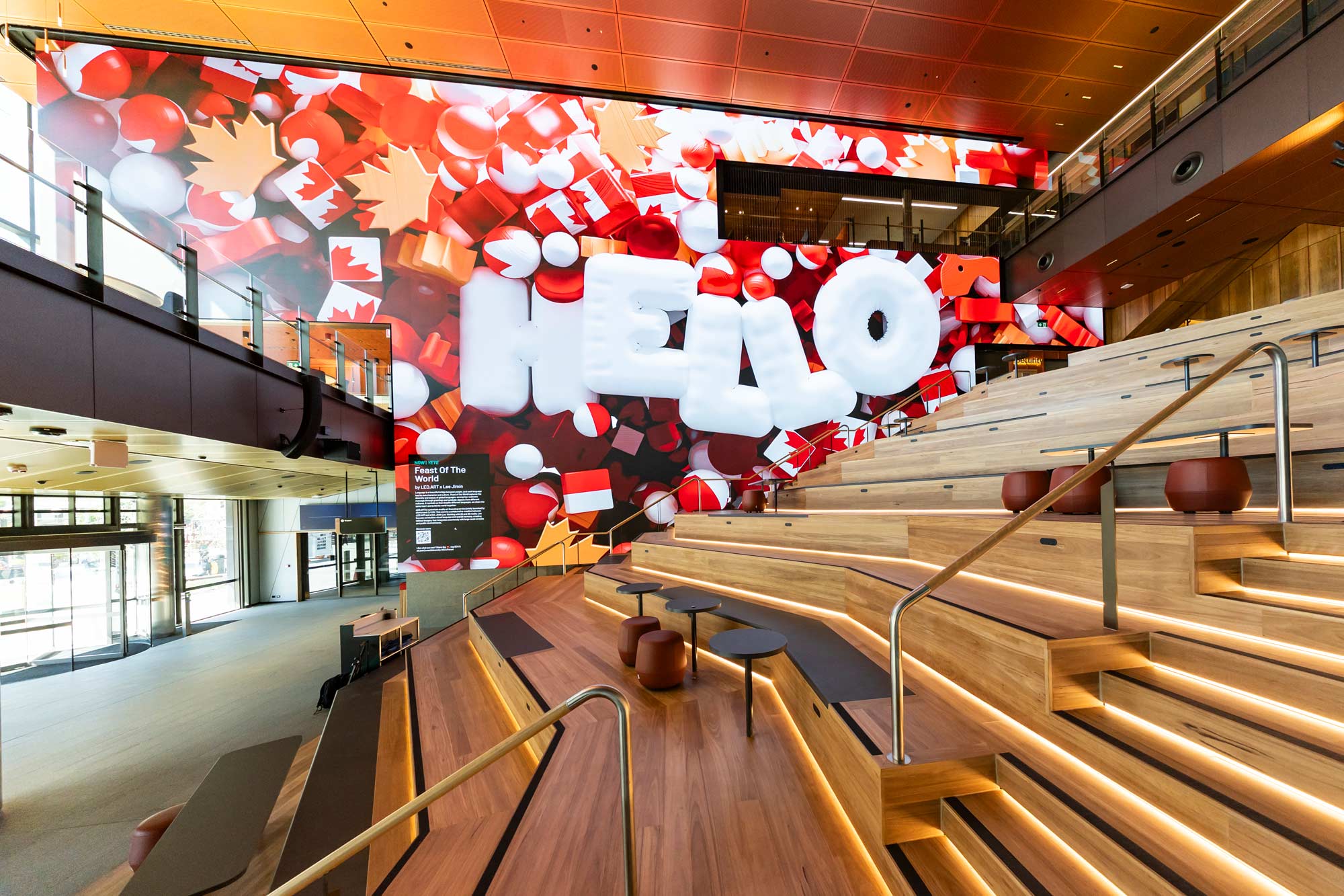 Building lobby with stairs and seating. A wall with a massive screen says 