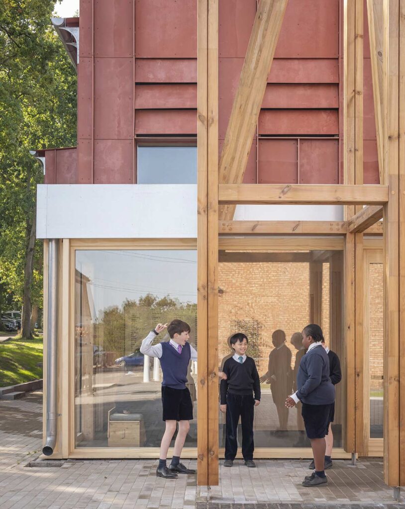 Students stand by the glass entryway and wooden structure.
