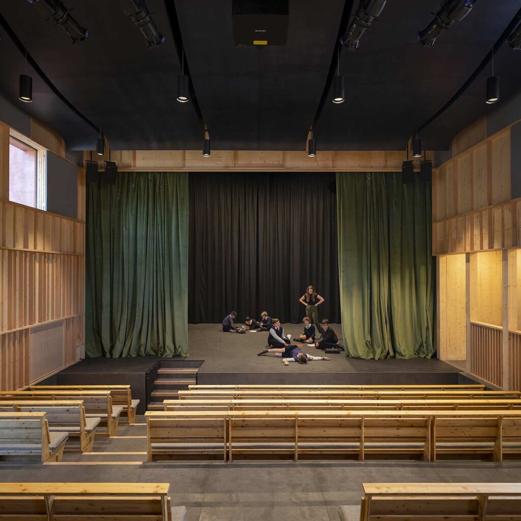 Students sprawl on the stage framed by green curtains and long benches.