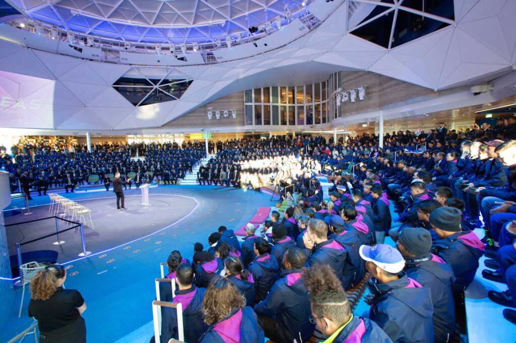 People watch a presenter at a podium in the sunlit dome.