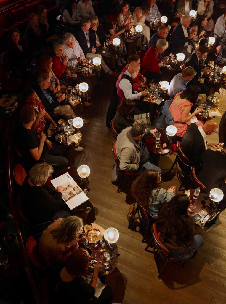 The audience enjoys food and beverage while looking on.