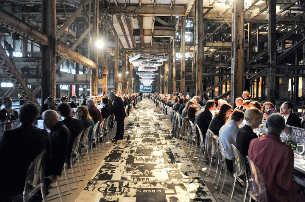 People dine at two long tables in the industrial interior.