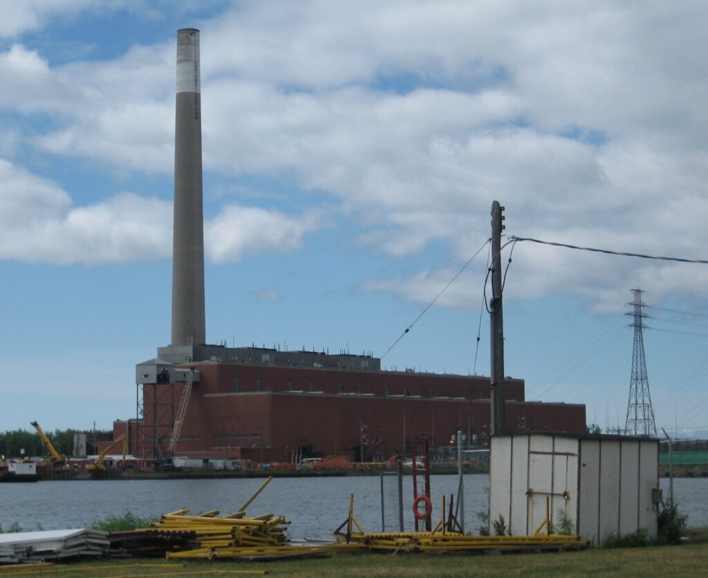 A power plant with smokestack alongside a waterfront.