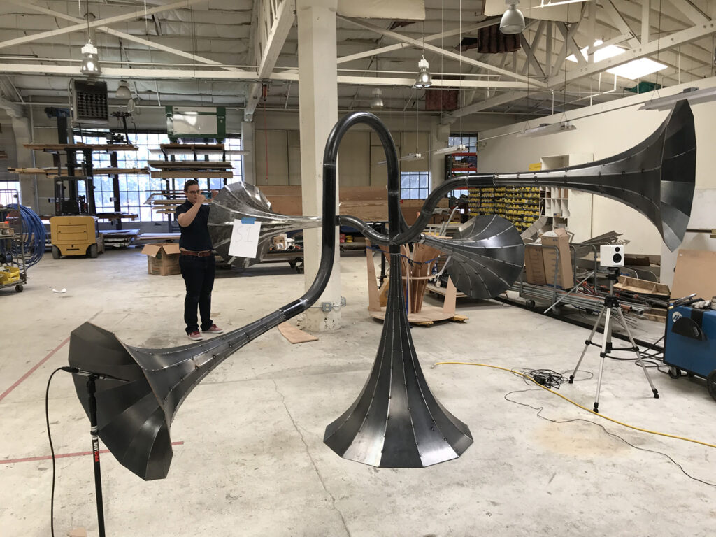 Audio monitoring equipment positioned around an unfinished metal horn structure in a fabrication studio.