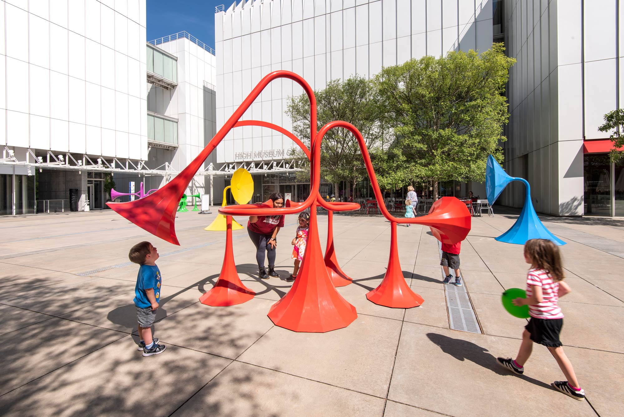 Small children play around a large orange sound sculpture.