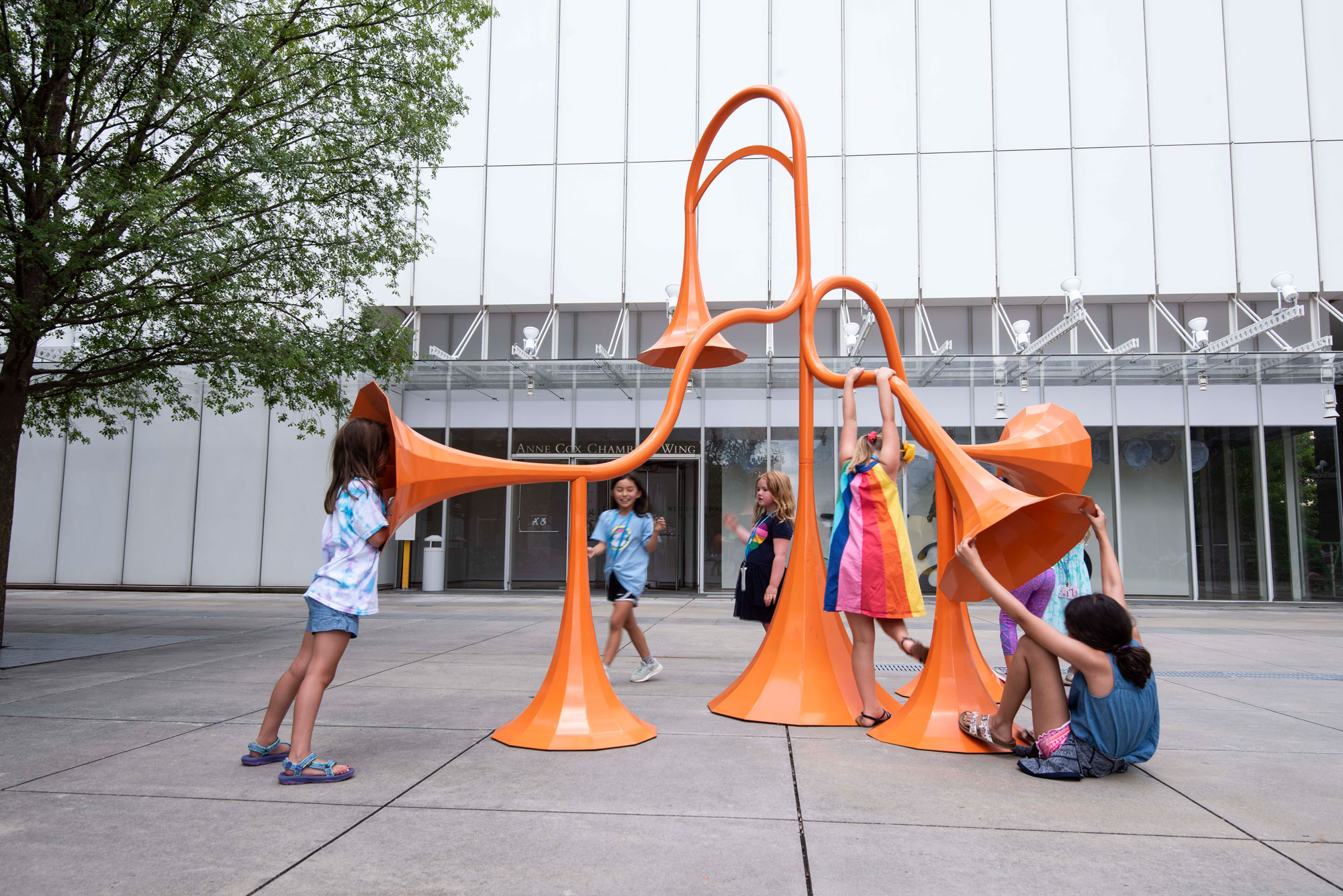 Children hang on the orange sound sculpture and speak into its horns.