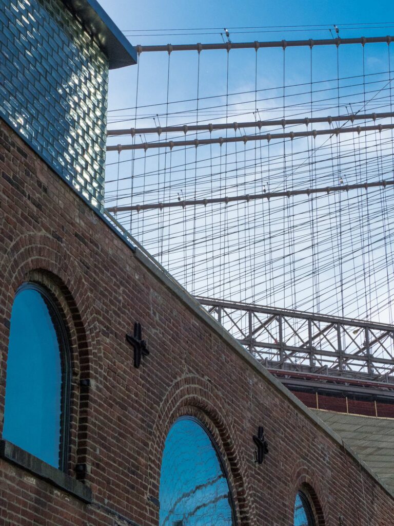 A detail shot of the brick and glass clerestory against the industrial bridge cables.