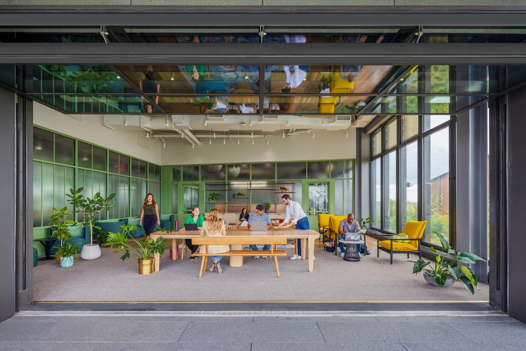 A gathering room with green walls and plants, an a garage door style wall that opens to the exterior.