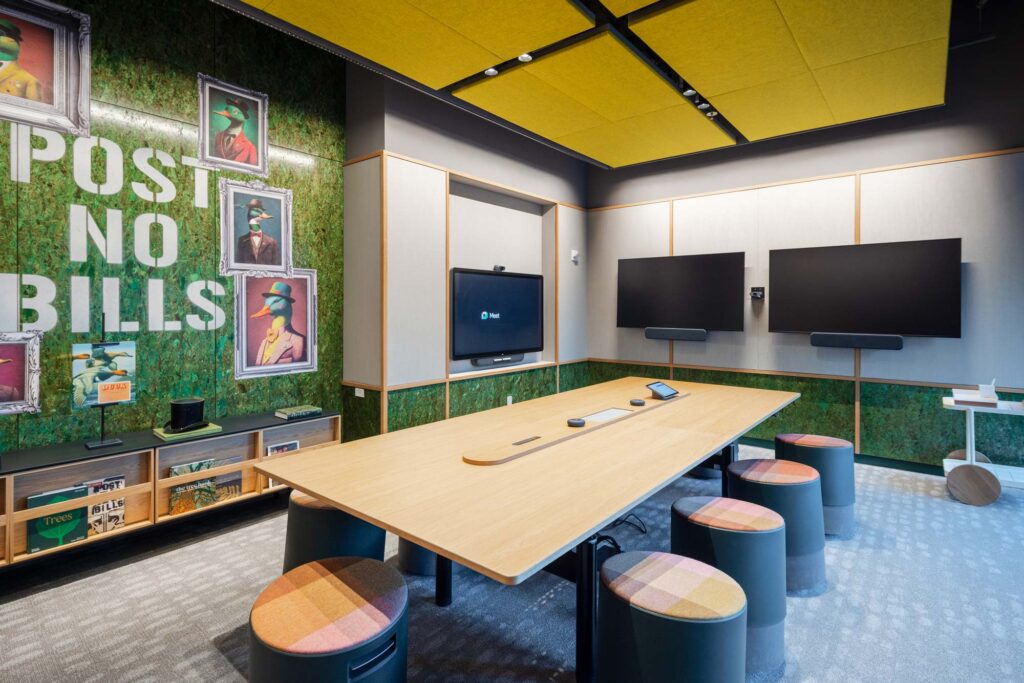 A meeting room with wall mounted screens. A mural on the wall reads Post No Bills.