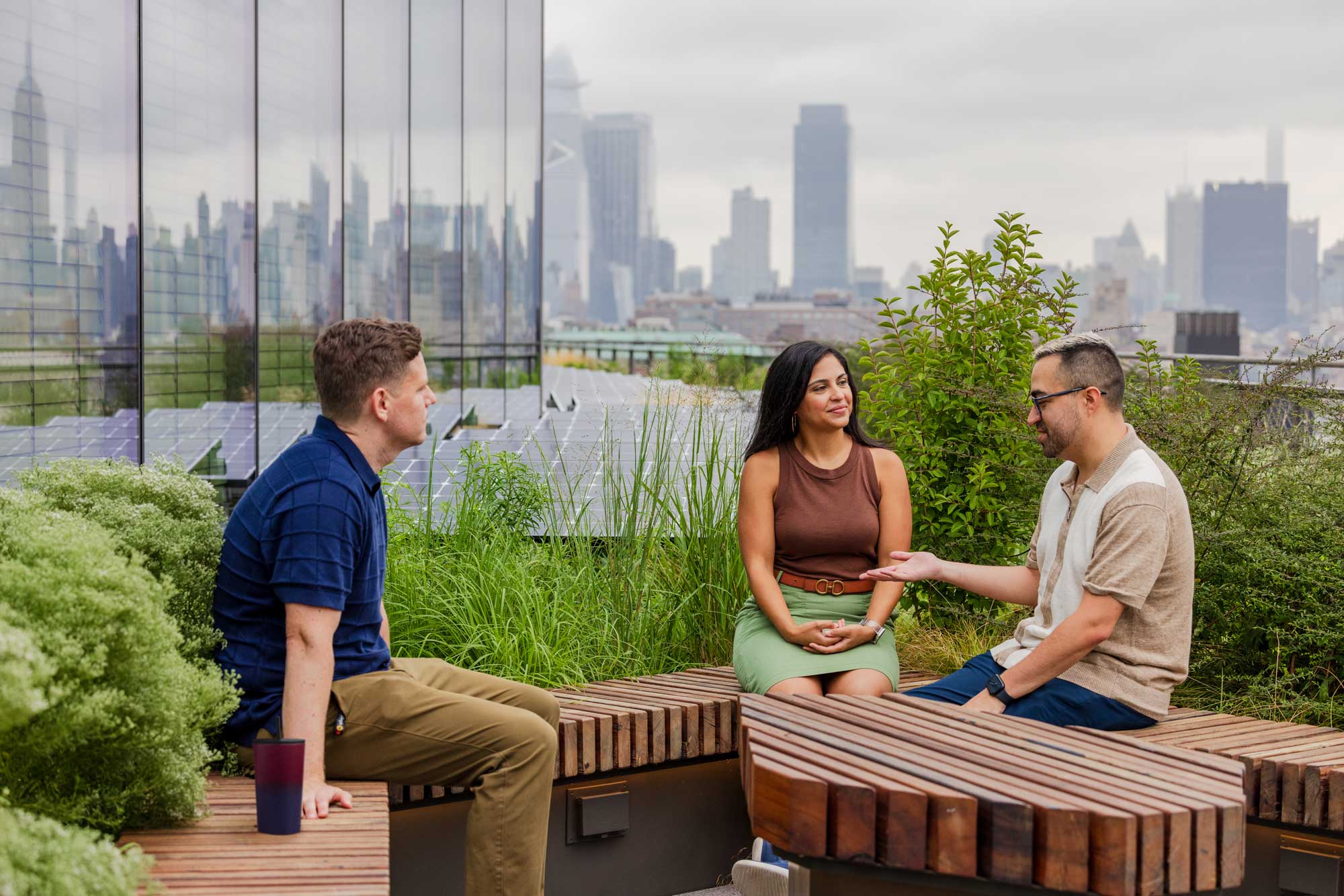 A group of people meet on benches on the roof, next to plants and solar panels.