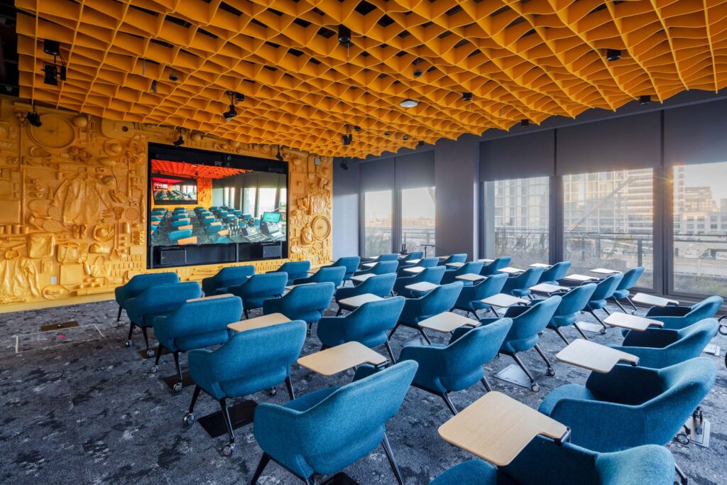 A classroom with dimensional yellow ceiling, and accent wall. A screen at the front mirrors the room.