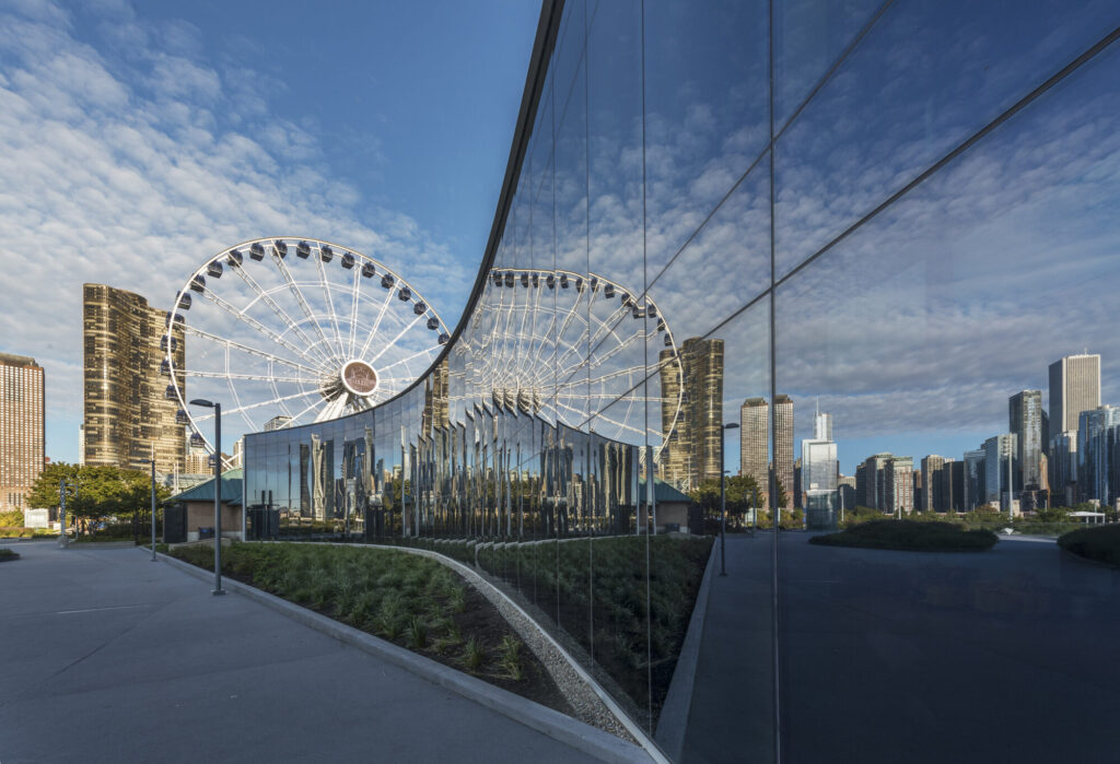 A curved glass exterior wall reflecting a ferris wheel.