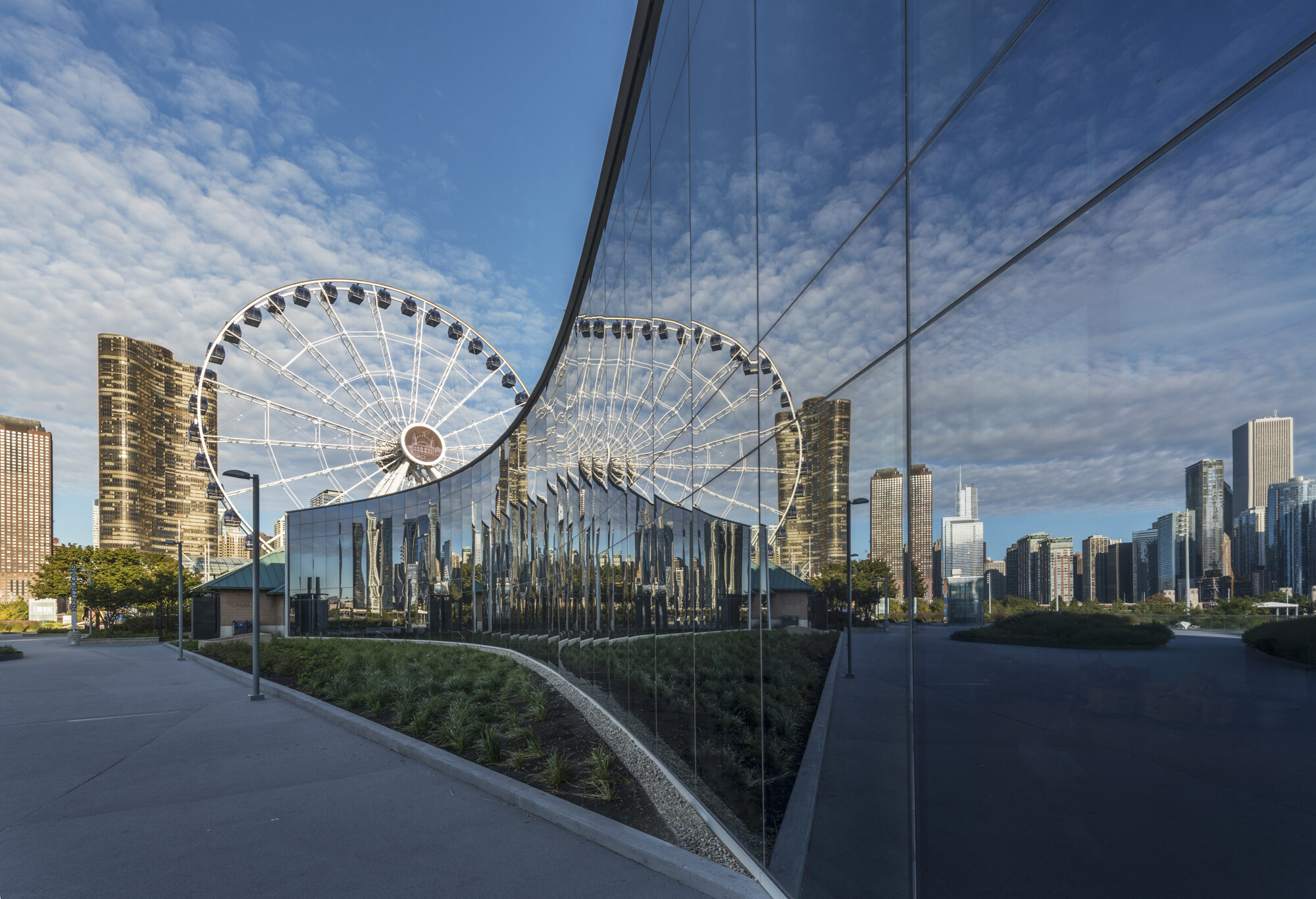 A curved glass exterior wall reflecting a ferris wheel.