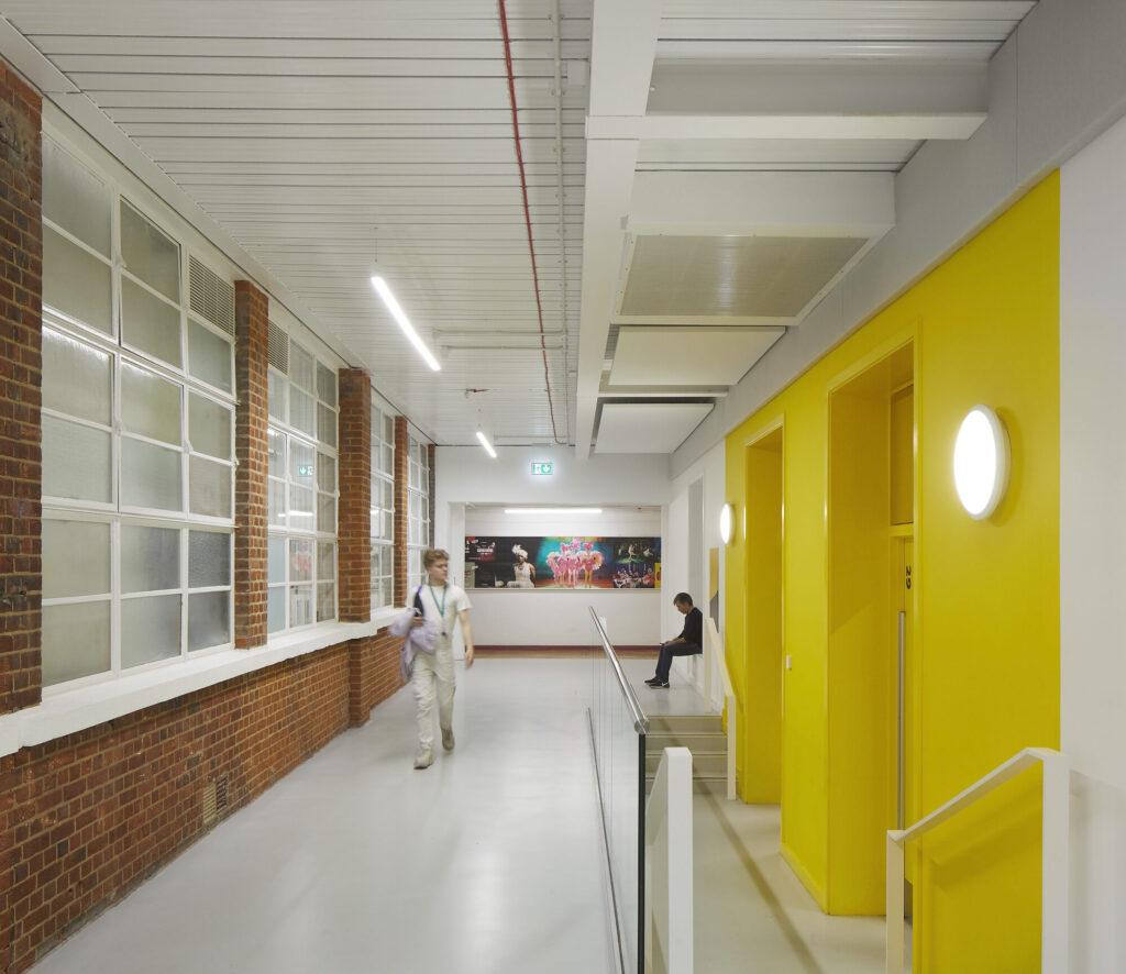 A student walks down a white hall opposite a yellow accent wall.