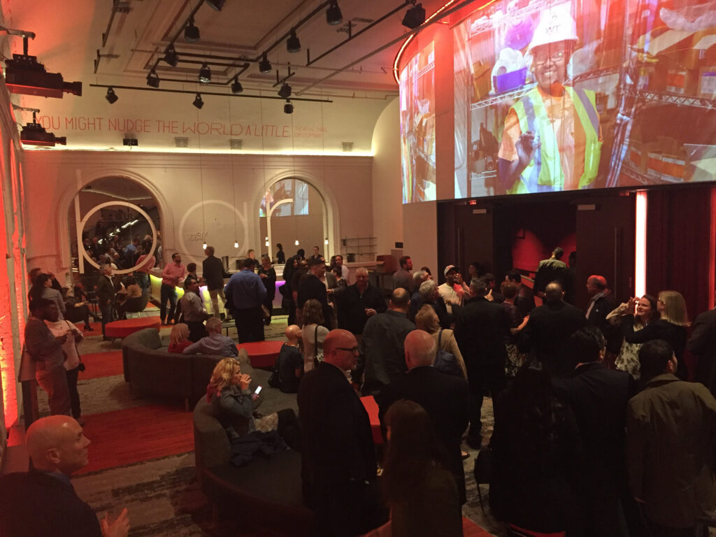 People at the bar and lounge at Baltimore Center Stage. A curved screen shows a projection of a construction worker.