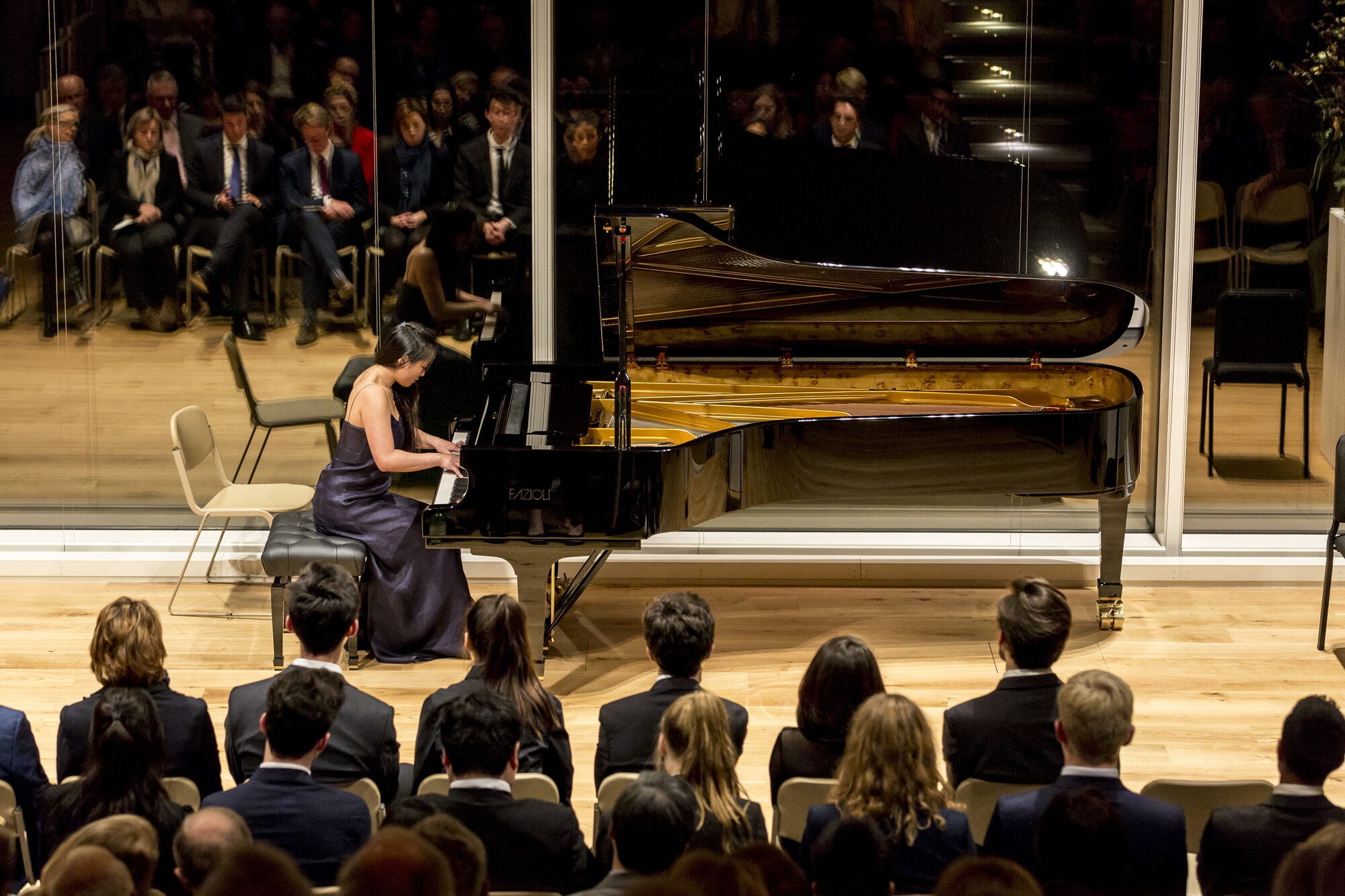A student plays piano in front of an audience at night.