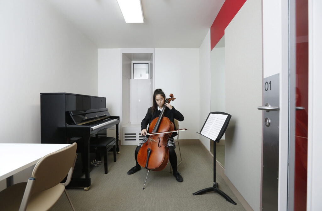 A student plays the cello in a rehearsal room.