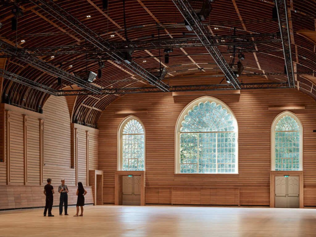 A wooden paneled room with three white, arched windows. The rounded ceiling is hung with technical equipment.