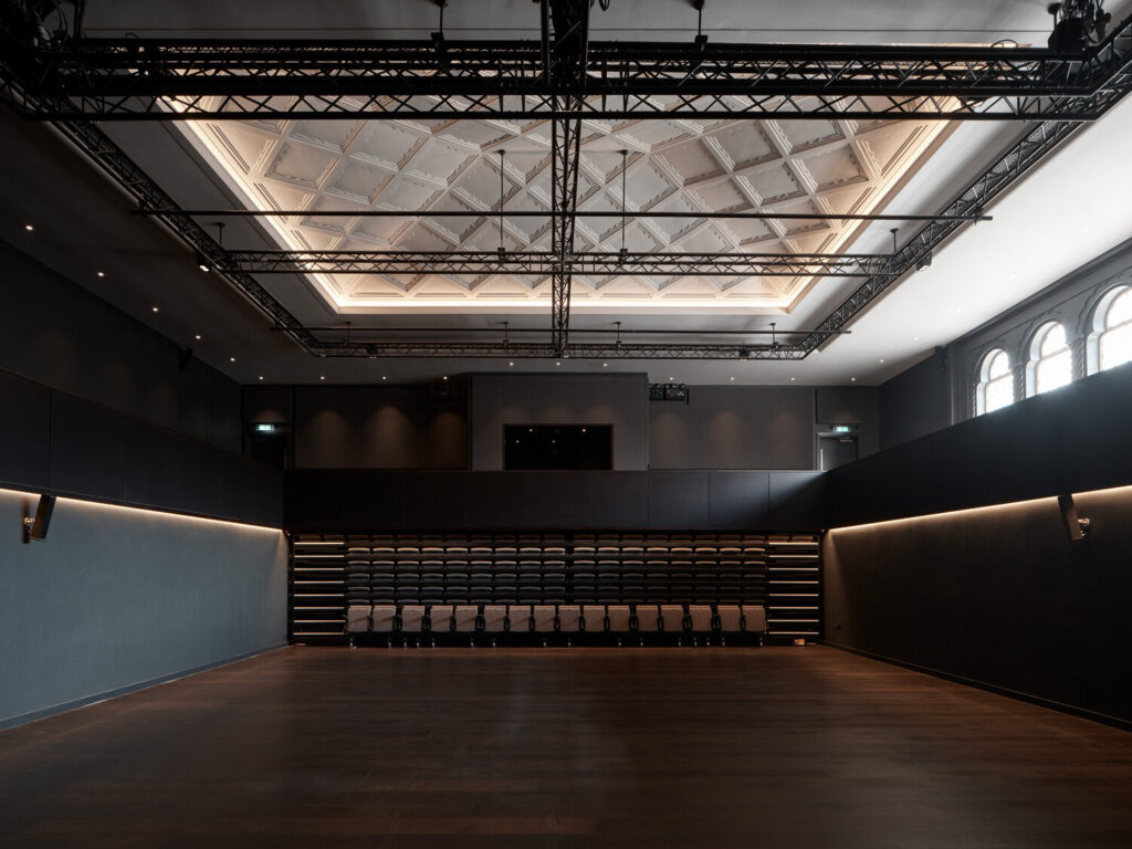 A rectangular room with flexible seating and low lighting. The ceiling has decorative moulding.