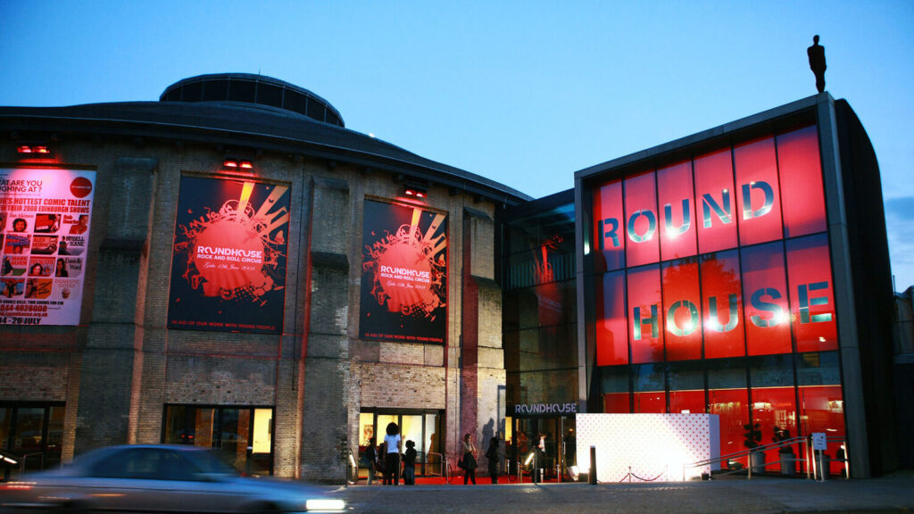 The exterior of the circular Camden Roundhouse building with red signage and banners.