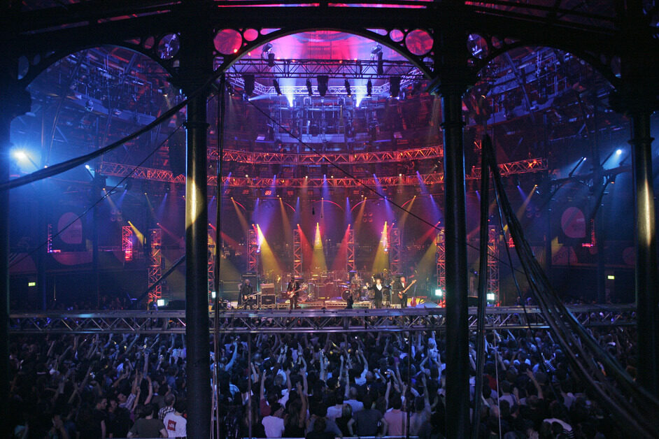 A band plays on stage while audience raises hands.