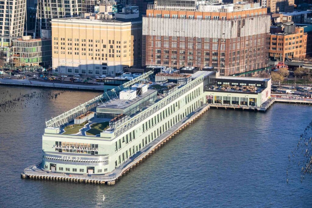The light green Pier 57 building juts out into the water. Seating and a green area are visible on the roof.