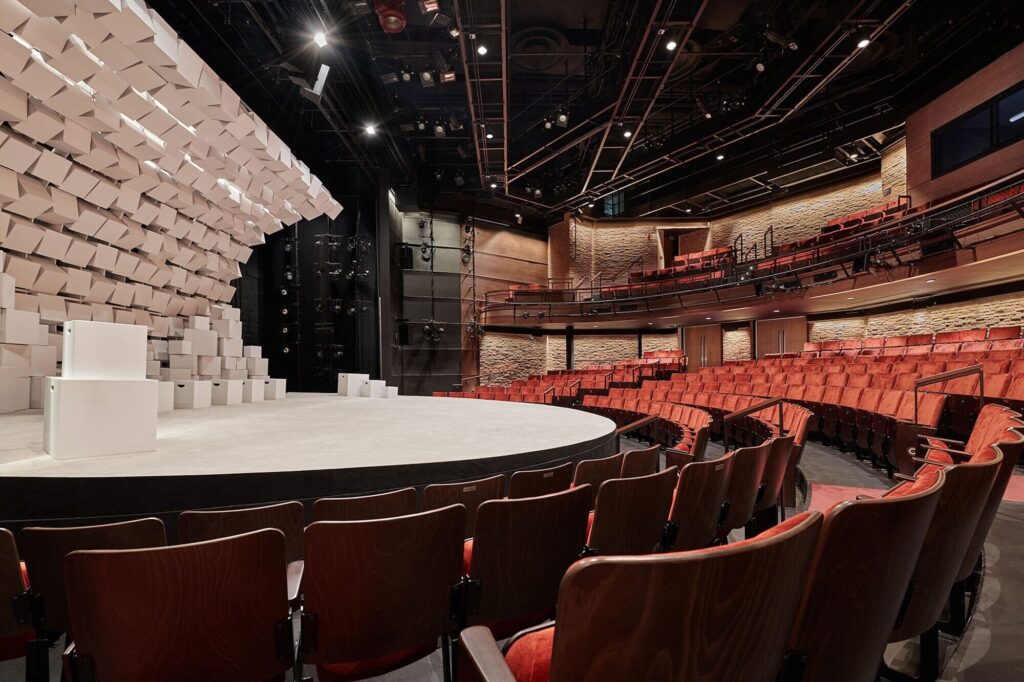 A round seating around circling a white stage with wavelike installation.
