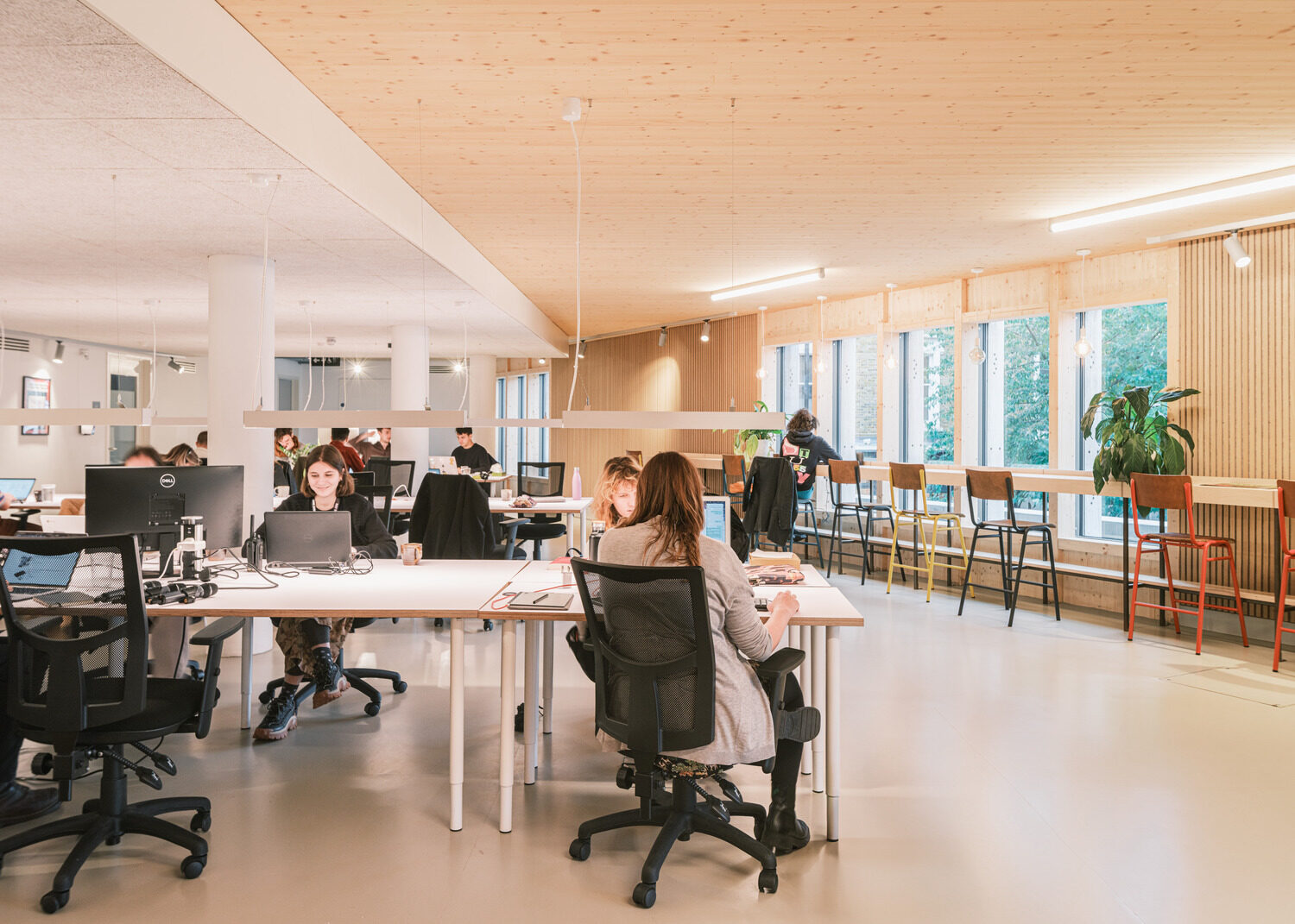 An open plan workspace with computers on the left and bar seating along a window on the right.